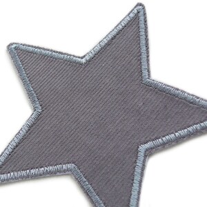 Puede incluir: Un parche gris en forma de estrella con un borde bordado azul claro.