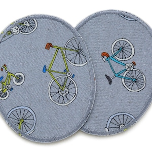 Könnte beinhalten: Zwei graue Stoffpatches mit weißem Rand. Jeder Patch zeigt ein sich wiederholendes Muster aus Fahrrädern in verschiedenen Farben. Die Fahrräder sind in einem einfachen, cartoonartigen Stil gezeichnet.