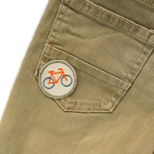 May include: A pair of khaki trousers with a patch of a bicycle on the back pocket.