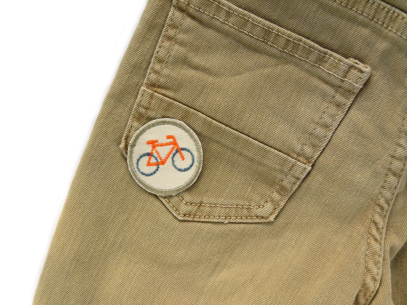 May include: A pair of khaki trousers with a patch of a bicycle on the back pocket.