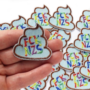 May include: A collection of 10 embroidered iron-on patches in the shape of a pile of poop with the letters "FCK NZS" in rainbow colors. The patches are on a white background.