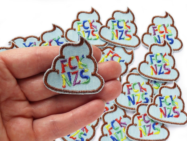 May include: A collection of 10 embroidered iron-on patches in the shape of a pile of poop with the letters "FCK NZS" in rainbow colors. The patches are on a white background.