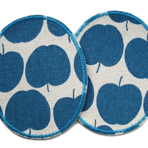 Könnte beinhalten: Zwei runde blaue und weiße Stoffuntersetzer mit einem sich wiederholenden Muster aus blauen Äpfeln auf weißem Hintergrund. Die Untersetzer haben einen blauen genähten Rand.