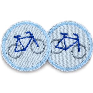 Op de afbeelding: Twee blauwe en grijze strijkbare fiets-patches op een witte achtergrond. De patches zijn rond en hebben een lichtblauwe rand.