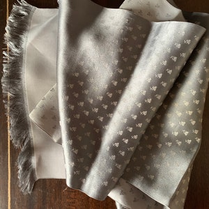 May include: A gray silk scarf with a white pattern of small leaves. The scarf has a fringed edge.