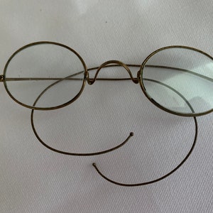 May include: A pair of vintage oval-shaped eyeglasses with a gold-tone metal frame and clear lenses. The glasses have a flexible wire temple.