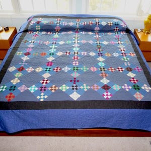 May include: A blue quilt with a geometric pattern of colorful diamond shapes. The quilt features a dark blue border and a lighter blue backing. The quilt is displayed on a wooden bed frame.