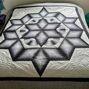 May include: A white and black quilt with a large, intricate star design in the center. The star is made up of smaller diamonds and squares, and the quilt is quilted with a swirling pattern.