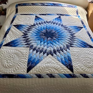 May include: A large, quilted bedspread featuring a central star design in shades of blue and white. The star is composed of diamond-shaped patches, surrounded by white squares with intricate, swirling patterns. The border is a mix of blue and white fabrics.