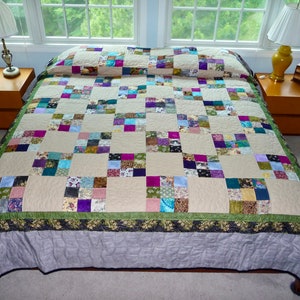 May include: A patchwork quilt with a beige background and squares of various colors, including purple, green, blue, and pink. The quilt has a green and black border and a gray underside.
