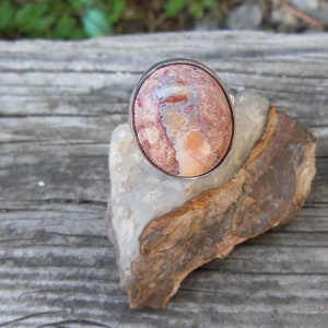 May include: A silver ring with a pink and brown oval-shaped gemstone set in a silver bezel.