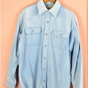 May include: A light blue long-sleeved denim shirt with a button-down front and two flap pockets on the chest.