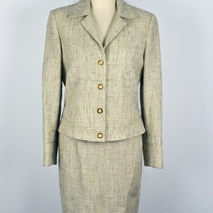Könnte beinhalten: Ein beige-schwarzer karierter Kostümrock mit goldenen Knöpfen. Die Jacke hat einen Kragen und lange Ärmel. Der Rock ist knielang.