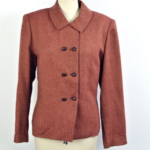 May include: A rust-colored blazer with a herringbone pattern and a double-breasted closure. The blazer has four buttons and a pointed collar.