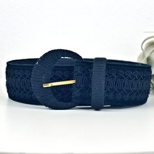 May include: A wide, navy blue velvet belt with an intricate embroidered design and a large, round, gold-toned buckle.