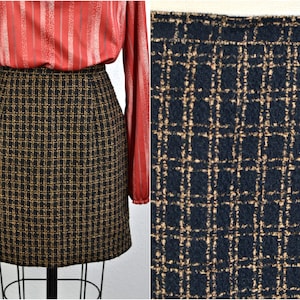 May include: A black and tan plaid mini skirt. The skirt is displayed on a mannequin. The fabric has a woven texture. The skirt is paired with a red blouse with vertical stripes.