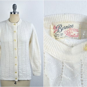 May include: White cardigan sweater with a button-up front and a label that reads "Bernice Creations by A.M. Knitwear Wintuk 100% Acrylic".