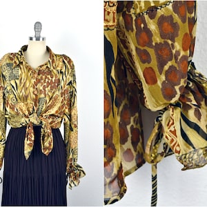 May include: A long-sleeved, button-up shirt with a brown, yellow, and black animal print. The shirt has a tie at the waist and ruffled cuffs.
