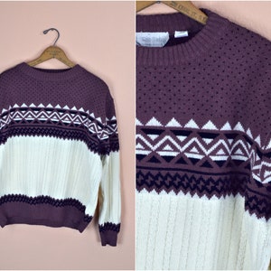 May include: A purple and white patterned sweater with a crew neck. The sweater has a geometric pattern in the colours purple, white, and black.