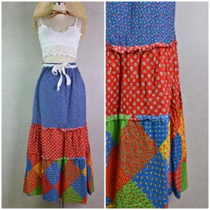 May include: A vintage patchwork maxi skirt with a white lace crop top. The skirt features a blue floral print, red polka dots, and a patchwork of colorful geometric and paisley patterns. The skirt has a white tie at the waist.