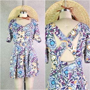 May include: A vintage-style dress with a colorful floral pattern in shades of purple, blue, orange, and white. The dress features short sleeves, a square neckline, and a pleated skirt. The back of the dress has a unique cut-out design.