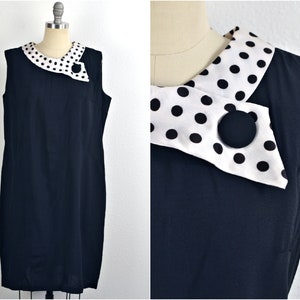 May include: A black sleeveless dress with a white and black polka dot collar. The collar is folded over and has a black button on the front.