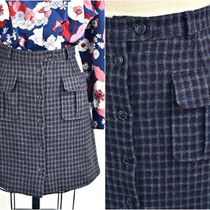May include: A blue and brown plaid skirt with a button front and two large pockets on the front. The skirt is made of a thick, textured fabric.