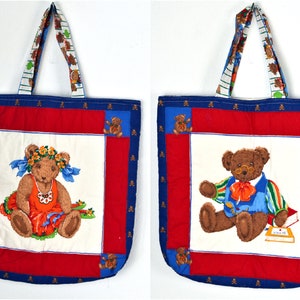 May include: Two quilted tote bags with blue and red trim. One bag features a teddy bear wearing a flower crown and a red dress. The other bag features a teddy bear wearing a blue shirt, red bow tie, and glasses. Both bags have a white background with small teddy bear designs on the straps.