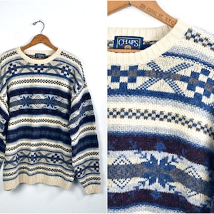 Puede incluir: Un suéter de color crema con un patrón de rayas azules, blancas y burdeos. El suéter tiene un diseño de copo de nieve y el nombre de la marca "CHAPS" es visible en la etiqueta.