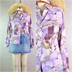 May include: A long-sleeved button-up shirt with a purple, white, and brown abstract print. The shirt has a collar and a button-up front.