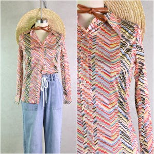 Puede incluir: Una camisa de manga larga con un estampado de chevrón colorido en rojo, amarillo, azul y negro. La camisa se exhibe en un maniquí con un sombrero de paja y una corbata de cuero marrón. La camisa se combina con pantalones vaqueros azules claros.