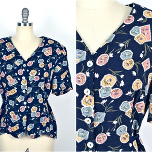 May include: A navy blue button-up blouse with a floral print featuring small, colorful squares. The blouse has a V-neckline and short sleeves.