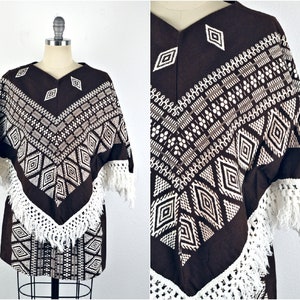 May include: A brown poncho with white geometric embroidery and fringe. The poncho has a V-neck and is made of a soft, woven fabric.