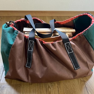 Könnte beinhalten: Eine große, rechteckige Tragetasche für Brennholz. Die Tasche ist hauptsächlich braun mit grünen Seitenteilen und einem roten Innenraum. Sie hat schwarze Griffe und ist mit Brennholz gefüllt.