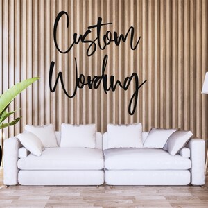 May include: A modern living room scene featuring a white sofa with several pillows, a black vase with a large green plant, and a wooden floor. The wall behind the sofa has vertical wooden panels, with the words "Custom Wording" in black script.