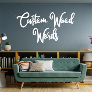 May include: A teal sofa with decorative pillows sits in front of a yellow bookshelf filled with books. Above the sofa, white cursive text reads "Custom Wood Words" on a blue wall. A table lamp and plants add to the decor.