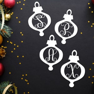 May include: Four white wooden Christmas ornaments with a cutout design. Each ornament features a different letter in a cursive font, spelling out the word "SAX".