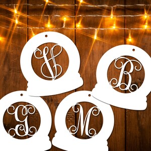 May include: Four white, round, paper ornaments with a decorative, cursive letter in the center of each. The ornaments are on a wood background with a string of lights.