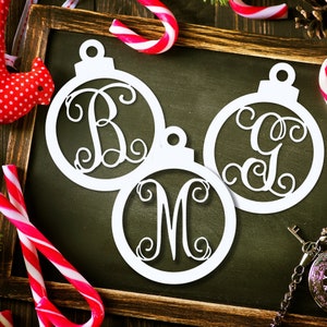 May include: Three white, cutout, Christmas ornament shapes with a monogram letter in each. The ornaments are on a black chalkboard background with a red and white candy cane and a small red bird.