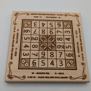 May include: Square wooden board game with etched numbers, dice, and instructions. The board features a grid of numbers, dice symbols, and text instructions around the edges. The game is designed for peg placement and dice rolling.