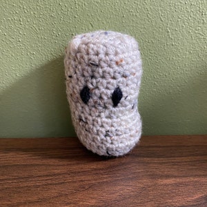 Puede incluir: Un fantasma de crochet con ojos negros. El fantasma es blanco con motas marrones y azules.