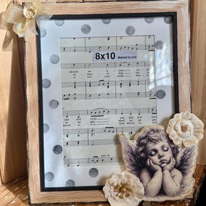 May include: Framed 8x10 inch print with sheet music, matted to 6x8 inches. The frame is light brown with a black inner border. A decorative angel and paper flowers adorn the frame. A gold bow is attached to the top left corner.