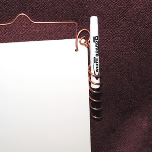 May include: A white dry-erase marker with the text "WHITE BOARD" is held in place by a copper wire coil. The marker is attached to a white board.