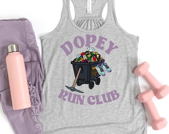 May include: Gray racerback tank top with the text "DOPEY RUN CLUB" in purple. The graphic features a mine cart filled with gems and sneakers. A pink water bottle, leggings, and dumbbells are also in the image.