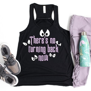 May include: Black racerback tank top with the text "There's no turning back now" in pink, surrounded by white eye graphics. The tank top is paired with gray athletic shoes, lavender leggings, and a floral water bottle.