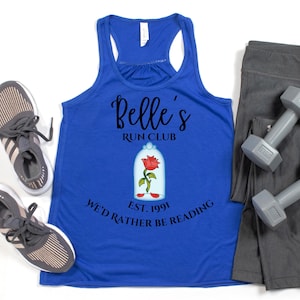 May include: A royal blue tank top with the text "Belle's Run Club" and a graphic of a rose in a glass dome. The text "We'd Rather Be Reading" and "Est. 1991" are also printed on the shirt. Gray athletic shoes, gray leggings, and dumbbells are also in the image.