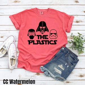 May include: A red t-shirt with a black graphic of three Star Wars characters, Darth Vader, Kylo Ren, and a Stormtrooper. The text "The Plastics" is printed below the characters.