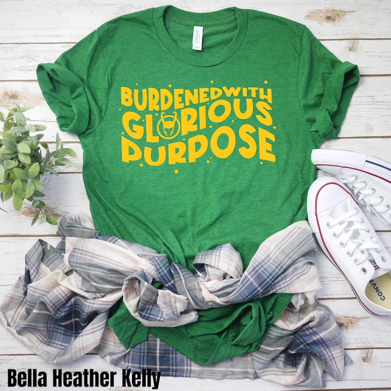 Puede incluir: Camiseta verde con el texto "burdened with glorious purpose" en letras amarillas. El texto incluye un peque&ntilde;o gr&aacute;fico de un casco con cuernos.
