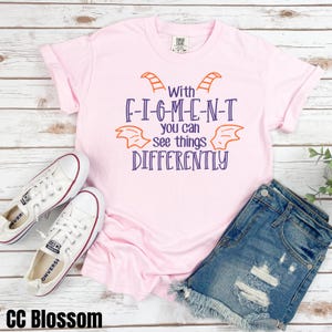 May include: A pink t-shirt with a purple and orange graphic that says "With F-I-G-M-E-N-T you can see things DIFFERENTLY".