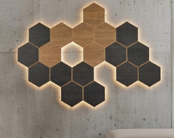 May include: A modern wall art piece composed of hexagonal tiles in shades of dark gray and light brown wood. The tiles are arranged in a honeycomb pattern, with a warm, glowing light outlining each tile, mounted on a concrete wall.